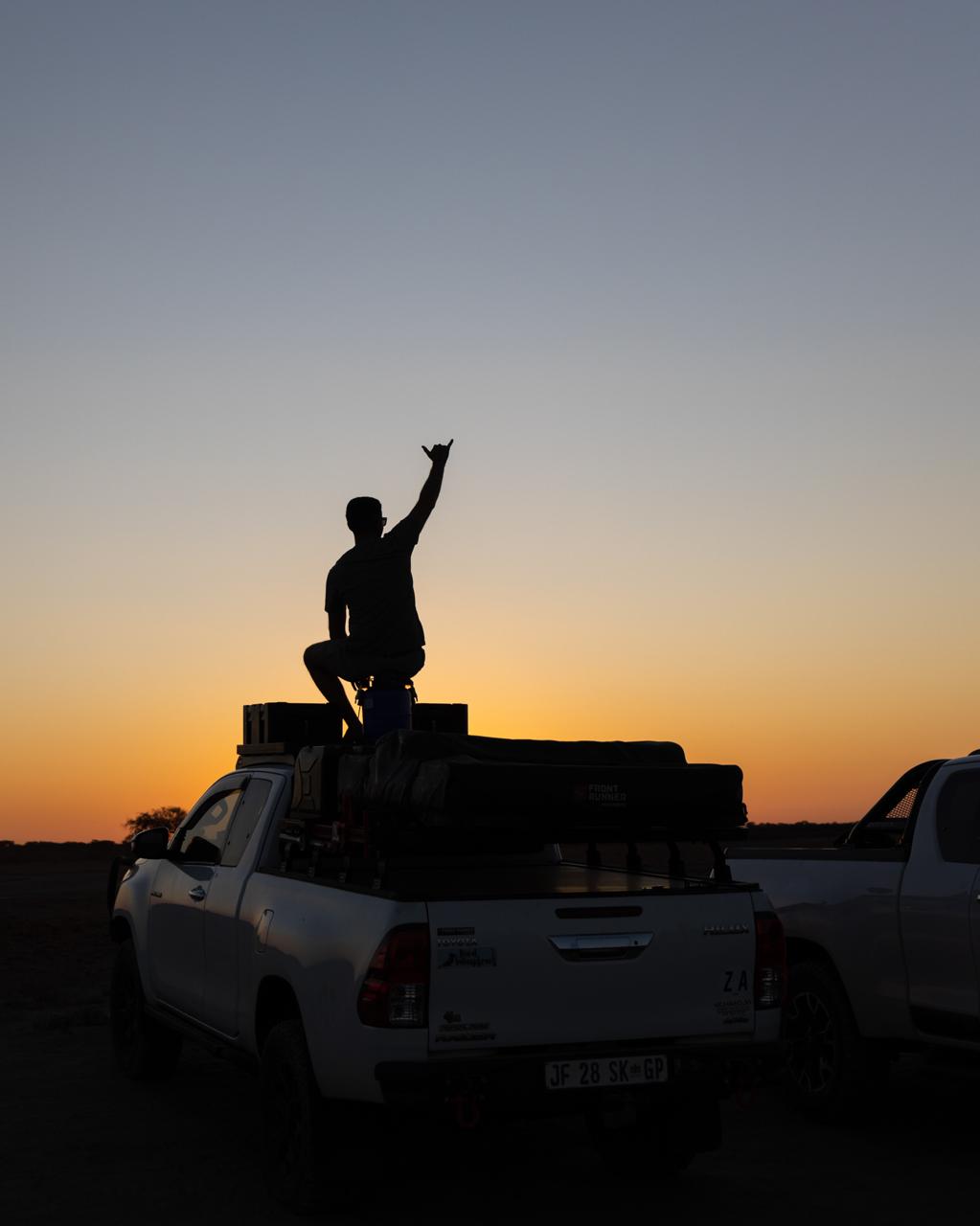A traveller watching sunrise from the roof of an overland vehicle